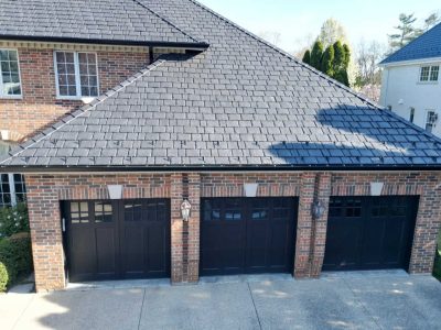 A three-car brick garage with black doors, attached to a brick house with a shingle roof, seen from above.