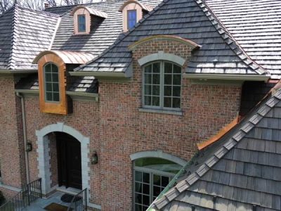 Two-story brick house with arched windows, shingled roof, two dormer windows, and a dark double front door.
